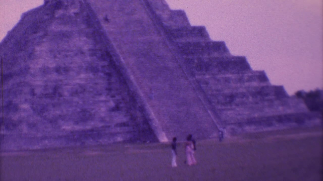 Tourists stand near the base of a large stepped pyramid with broad stairs.