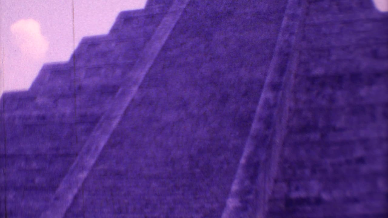 1973 8mm-style view of El Castillo with a steep stairway, stepped stone tiers, purple color cast, and pale sky.