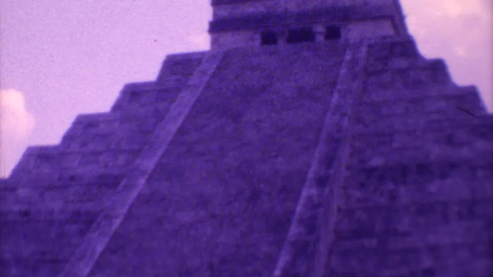 The camera frames El Castillo from below, showing the broad stairway, stepped sides, summit structure, and faded purple 8mm color.