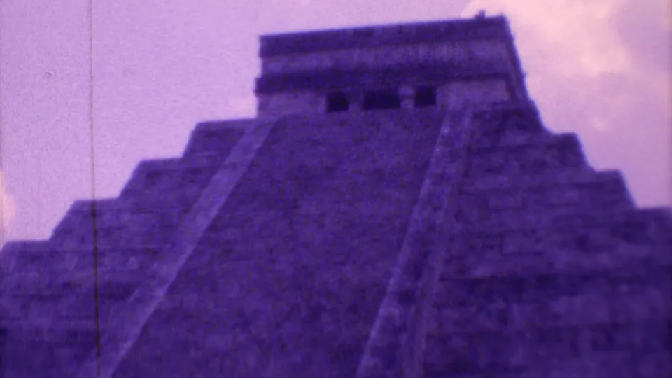 Purple-faded 8mm frame of El Castillo, emphasizing the upward stairway, terraced stone form, and dark openings near the top.