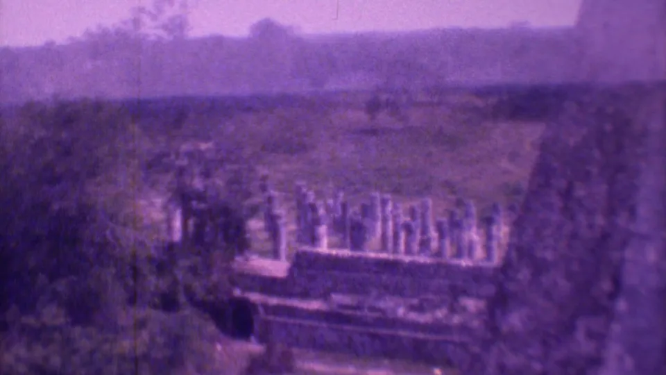 Purple-tinted 8mm frame showing a cemetery terrace or path, rows of grave markers, dark trees, and distant hillside in Mexico City.