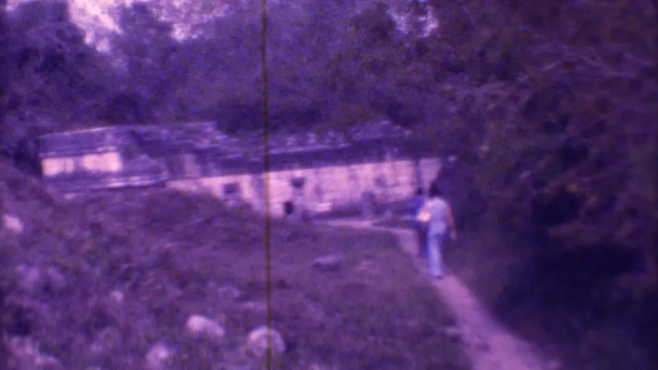 In the Mexico City home-movie frame, people appear near a wooded path leading to a low masonry building.