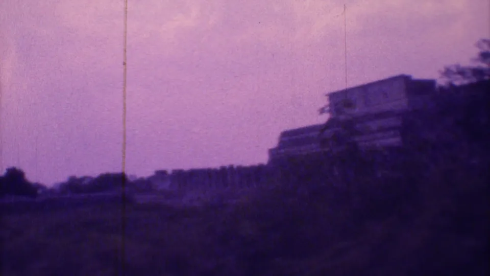 1973 Mexico City home-movie frame showing a distant pyramidal monument, open hilly ground, trees, and purple-shifted 8mm color.
