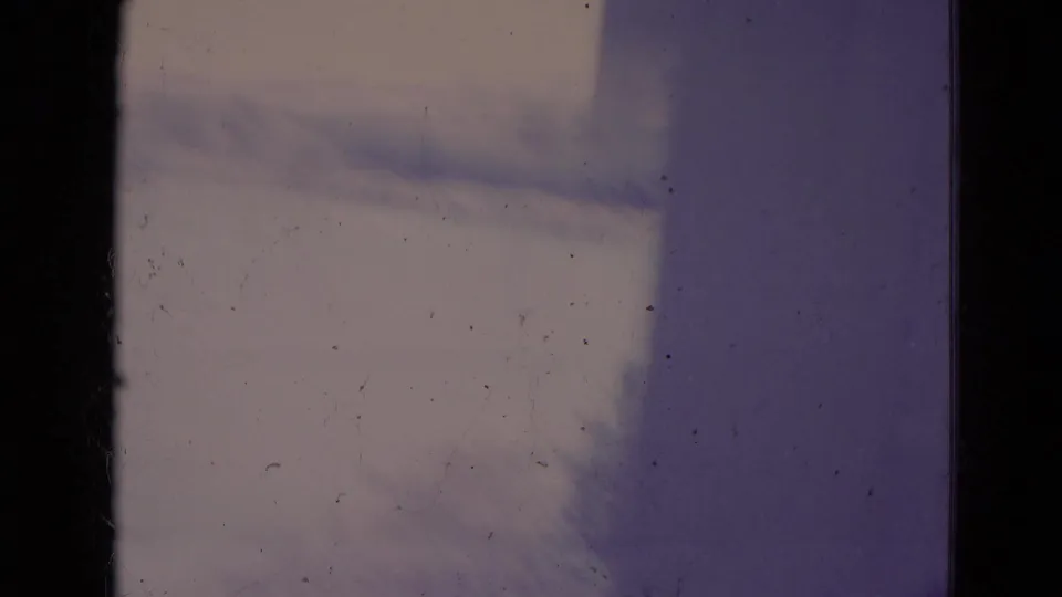 Soft, overexposed 8mm frame from the Orlando home movie, showing indistinct pavement or walkway and a dark edge of the scan.