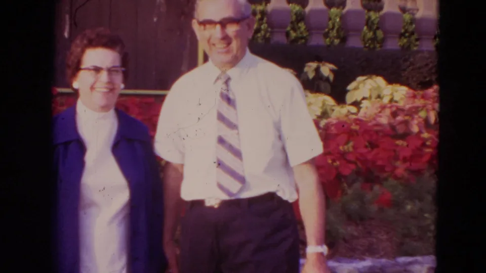 The couple faces the camera and smiles in the 1974 Orlando garden scene, framed by red flowers and a wooden fence.