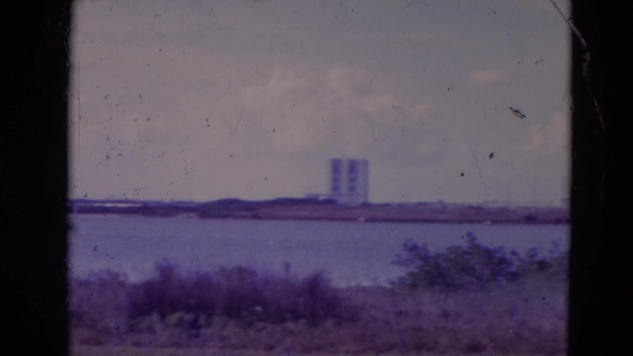 1974 Orlando-area 8mm frame showing a distant white tower beyond water, scrub vegetation, cloudy sky, and dark film borders.