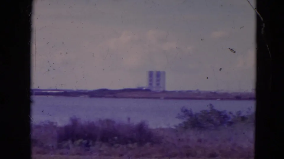 1974 Orlando-area 8mm frame showing a distant white tower beyond water, scrub vegetation, cloudy sky, and dark film borders.