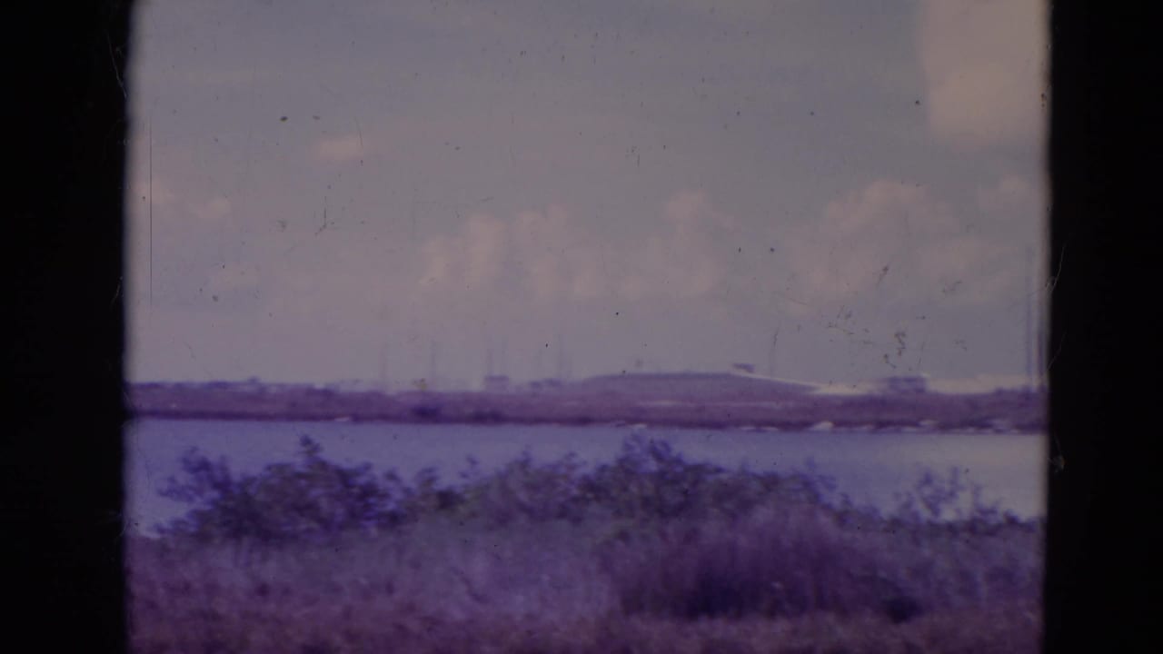 1974 Orlando-area 8mm frame with a low stadium-like structure on the far shore, water, brush, and visible film wear.