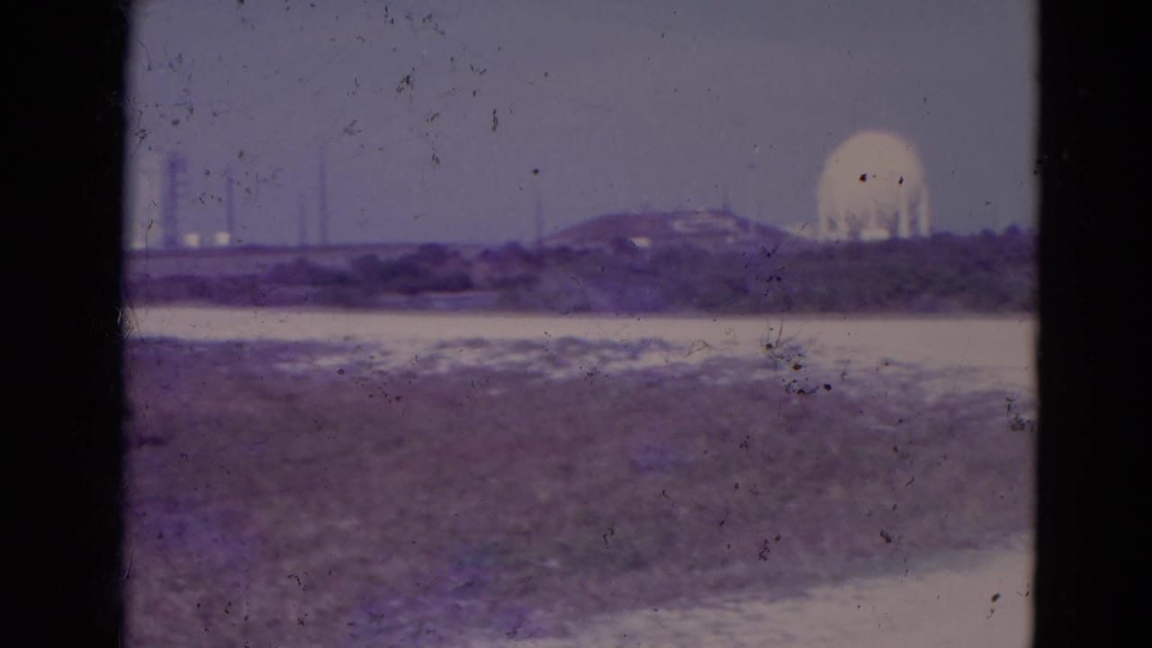 1974 Orlando-area 8mm frame with a white dome, distant vertical towers, low horizon buildings, and sparse open terrain across the foreground.