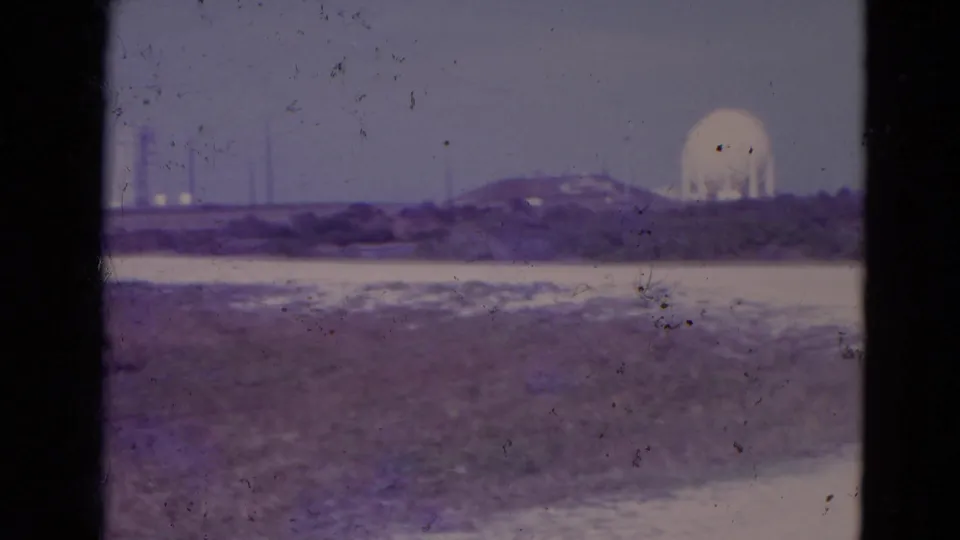 1974 Orlando-area 8mm frame with a white dome, distant vertical towers, low horizon buildings, and sparse open terrain across the foreground.