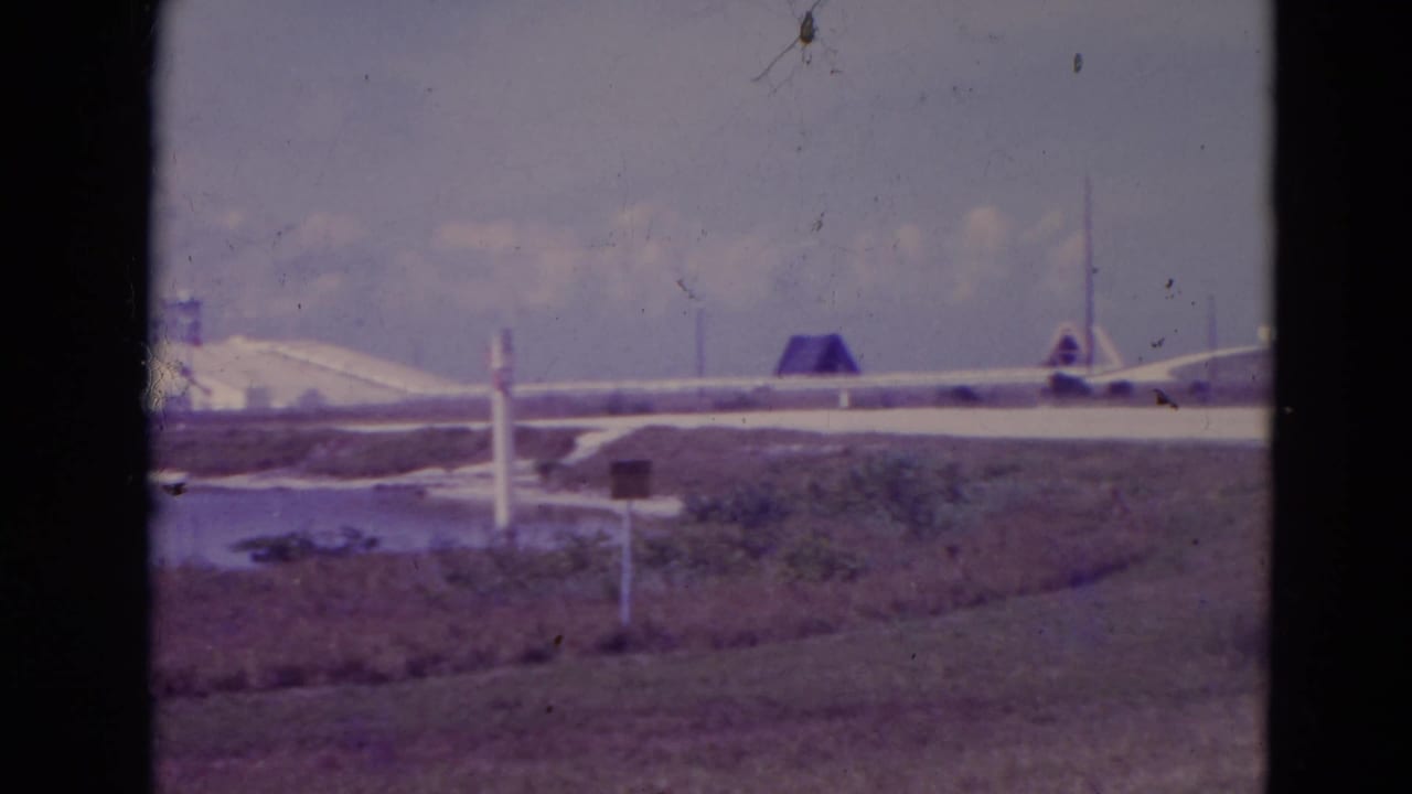 Distant launch pad structures across marshland under a bright sky.