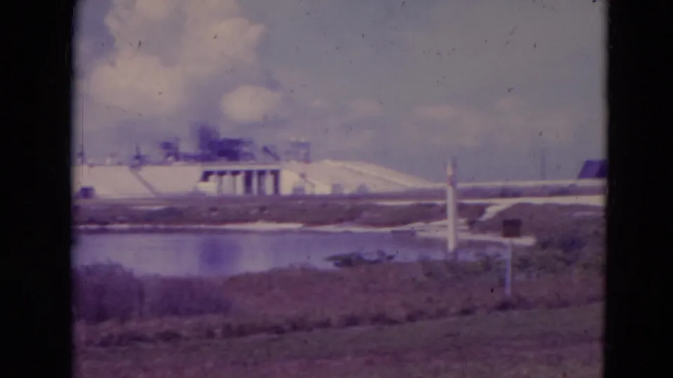 Visitor-shot 1974 view of Cape Canaveral launch pad structures beyond water and low marsh vegetation.