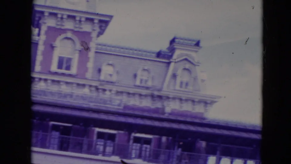 1974 Orlando home-movie frame angled upward at the Disney entrance roofline, dormer windows, balcony, and open sky.