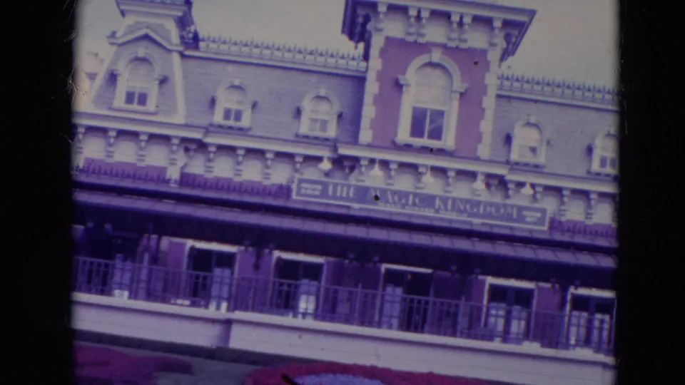 1974 Orlando 8mm frame showing the Disney entrance building, visible sign band, balcony, roof details, and flower bed at the base.
