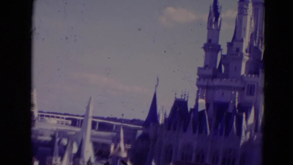 1974 Orlando 8mm frame showing Cinderella Castle spires, nearby flags, and background resort architecture.
