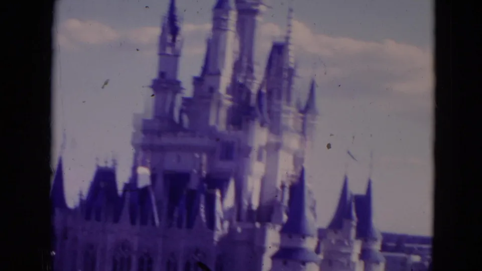 1974 Orlando home-movie frame centered on Cinderella Castle spires, with soft focus, film dust, and dark 8mm borders.