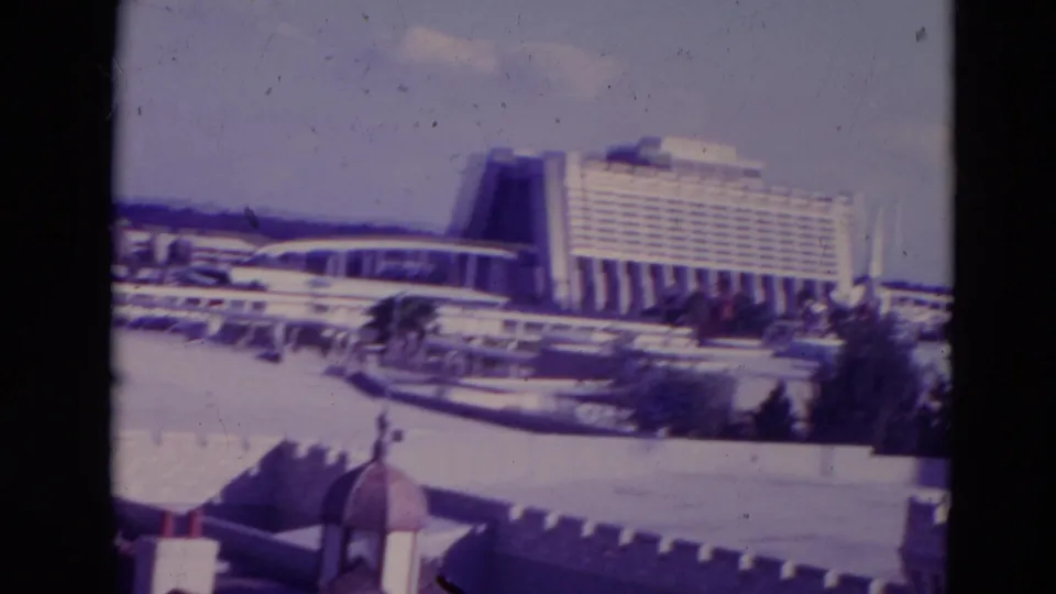 1974 Orlando view toward a large modern resort hotel, with white themed rooftops, parapets, trees, and elevated track in the foreground.