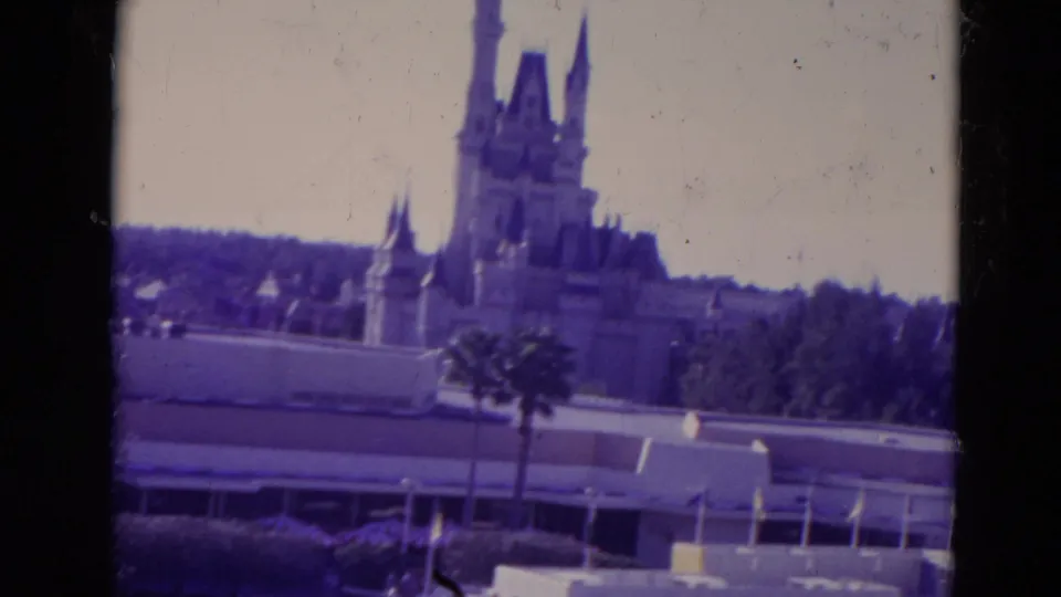 1974 Orlando 8mm frame showing castle spires, a palm tree, low buildings, railings, and soft purple archival color.