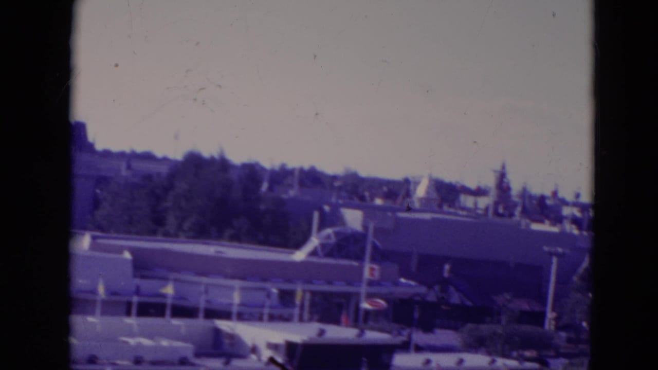 1974 Orlando theme-park view with low attraction buildings, treeline, rooflines, and a hazy distant skyline.