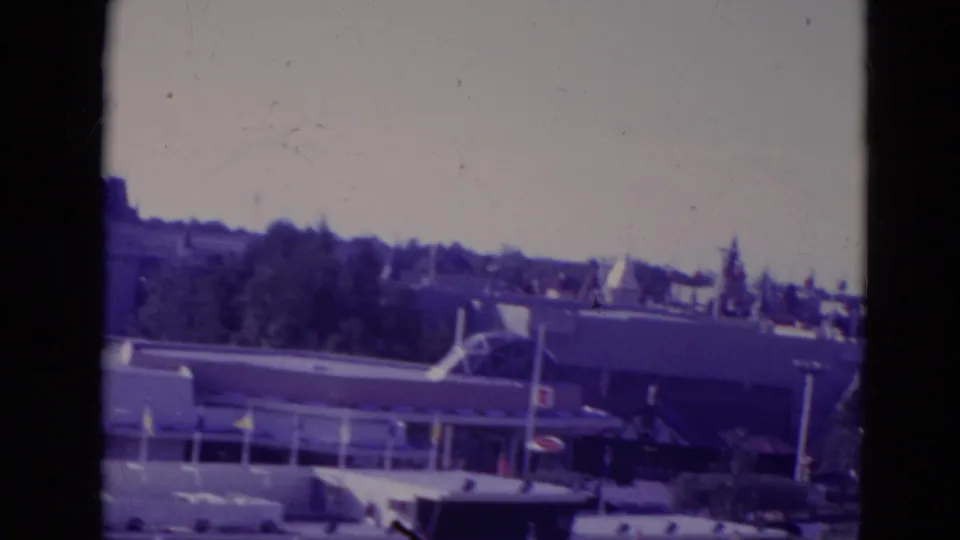 1974 Orlando theme-park view with low attraction buildings, treeline, rooflines, and a hazy distant skyline.