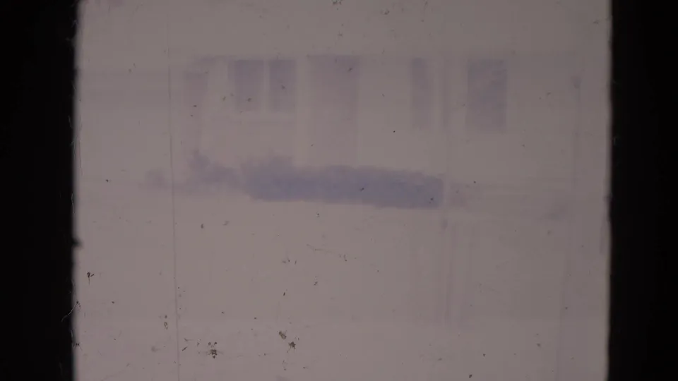 Hazy 1974 Orlando home-movie frame looking through a window toward a snow-covered suburban house and yard.