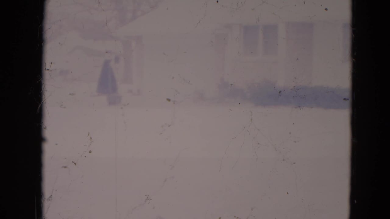 Soft view of a house beyond a dark window divider with snow in the yard.