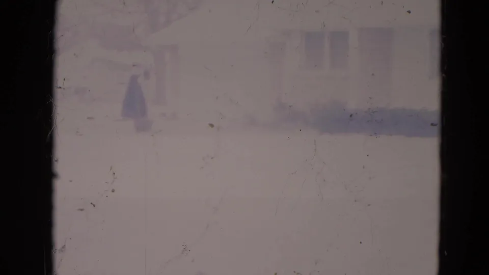 Soft 8mm frame of a snowy Orlando suburban house seen past a dark vertical window divider.