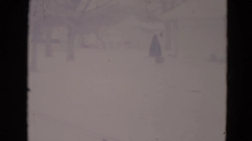Overexposed 1974 Orlando frame with a dark-coated figure walking across a snowy residential yard.