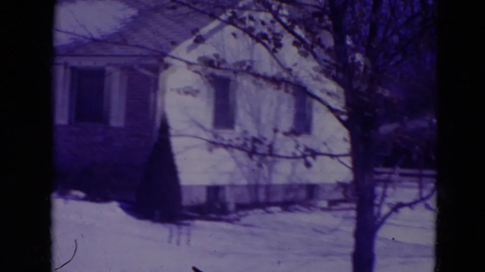 Purple-tinted 8mm frame of a snow-covered Orlando suburban house with bare branches and a yard in front.
