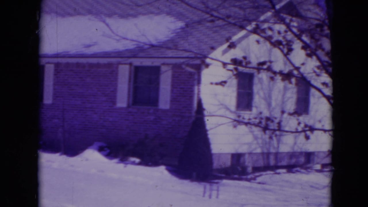 1974 Orlando home-movie frame showing a snow-covered suburban ranch house with brick facade, white siding, and bare tree branches.