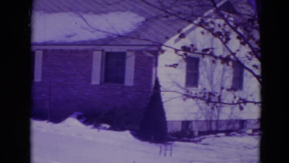 1974 Orlando home-movie frame showing a snow-covered suburban ranch house with brick facade, white siding, and bare tree branches.