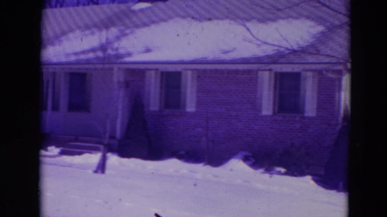 1974 Orlando frame of a quiet suburban house exterior with snow on the roof and yard, front steps, and shuttered windows.