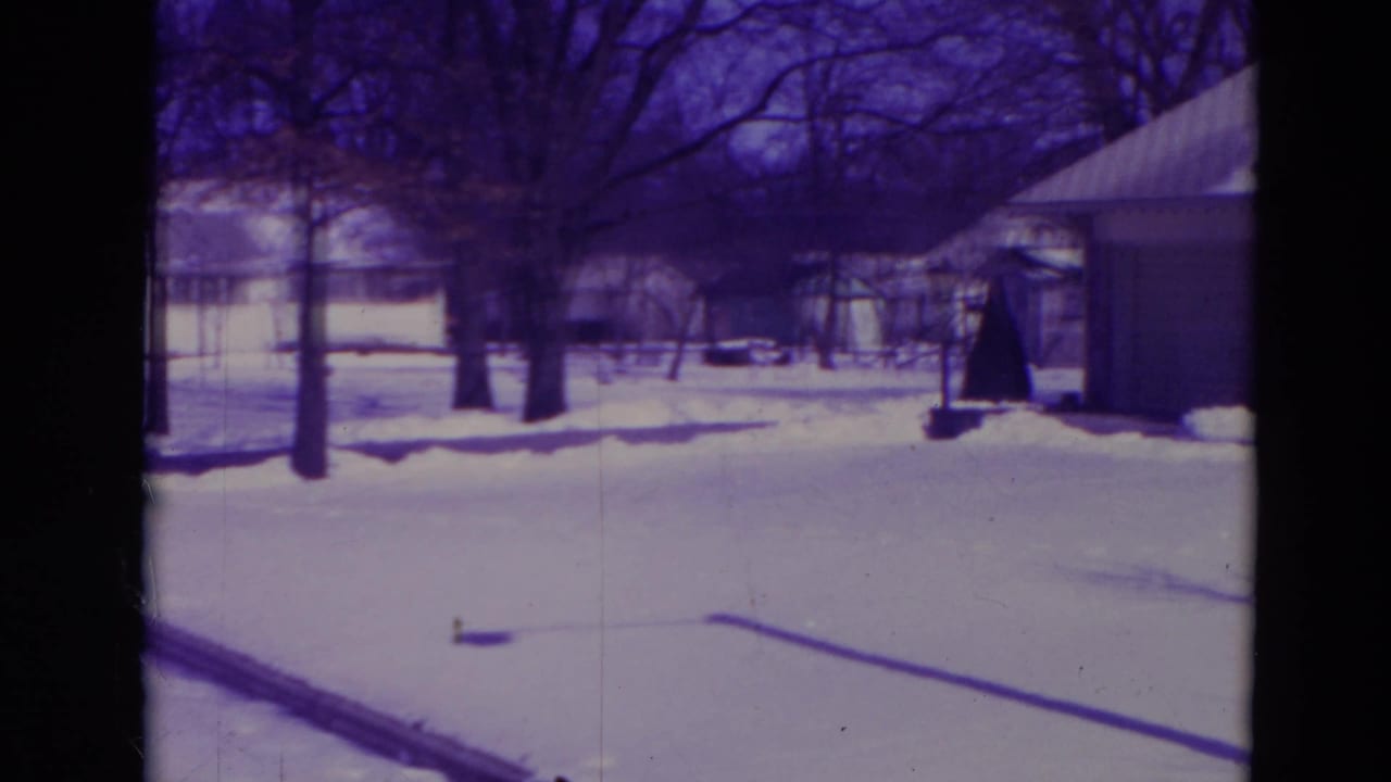 1974 Orlando 8mm frame of a snow-covered suburban street area with bare trees, low houses and garages under winter light.