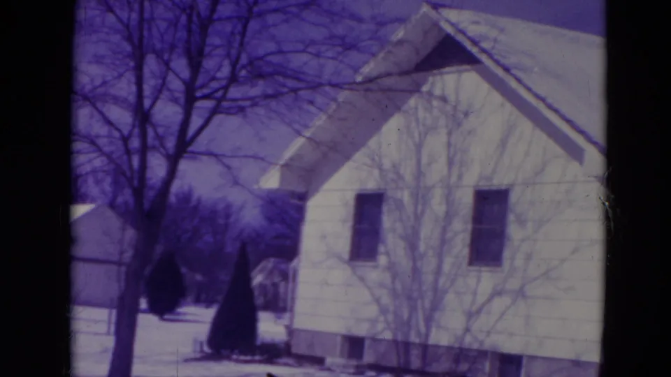 1974 Orlando home-movie frame showing a white single-story house, snow-dusted roof, bare trees and a snow-covered yard.