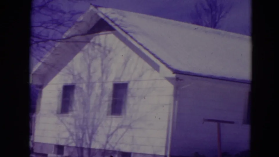 1974 Orlando 8mm frame of a white residential house with snow on the roof, bare branches across the facade and snow on the ground.