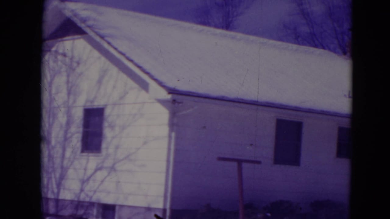Snow-covered white house exterior with bare trees and dark frame edges.