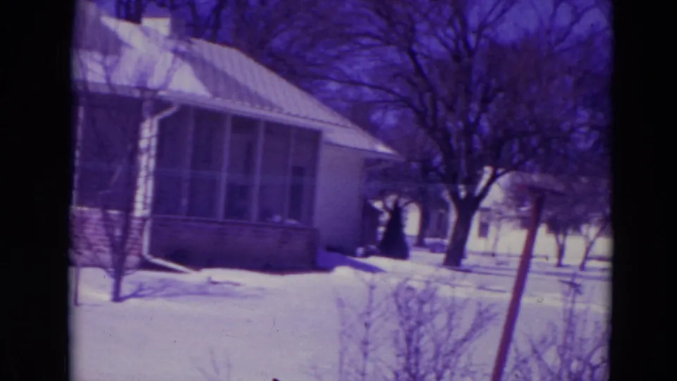 1974 8mm frame from Orlando showing a snowy suburban yard, a one-story house, bare trees, and neighboring homes.