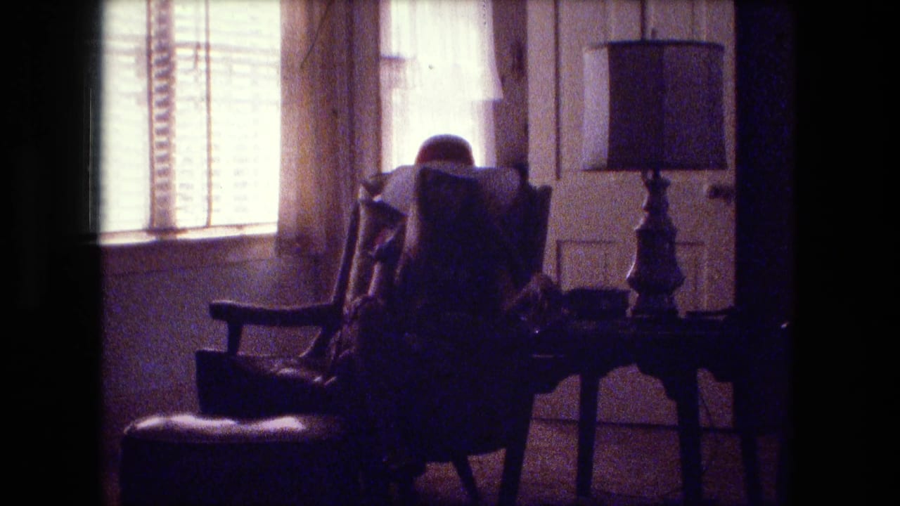 A dim 1974 Fort Wayne interior shows a person seated by a window with blinds, curtains, a side table, and a lamp.