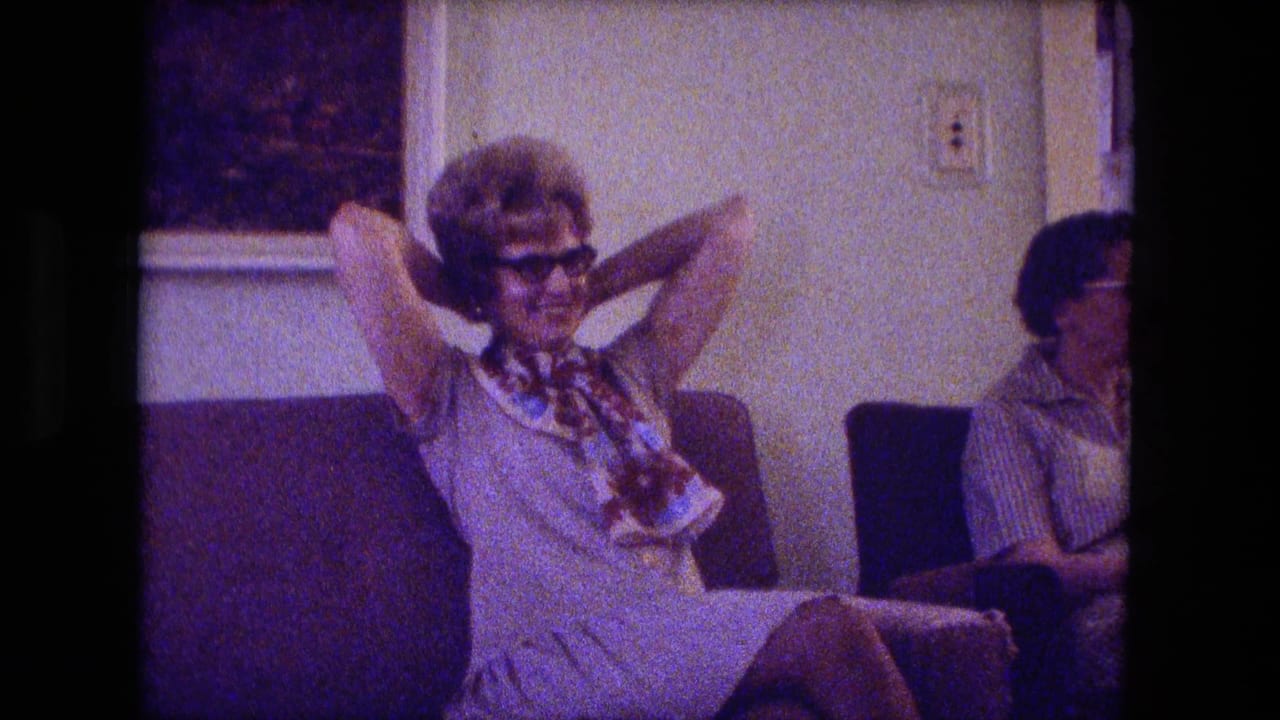 Fort Wayne 1974 living-room frame with a woman in sunglasses reclining on a couch and another adult seated nearby.