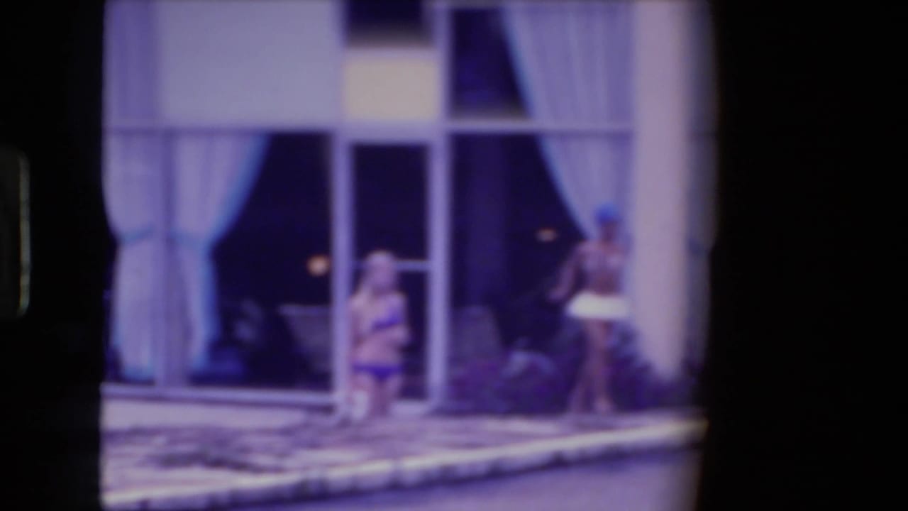 A woman in a bikini stands near the pool while another person passes at right.