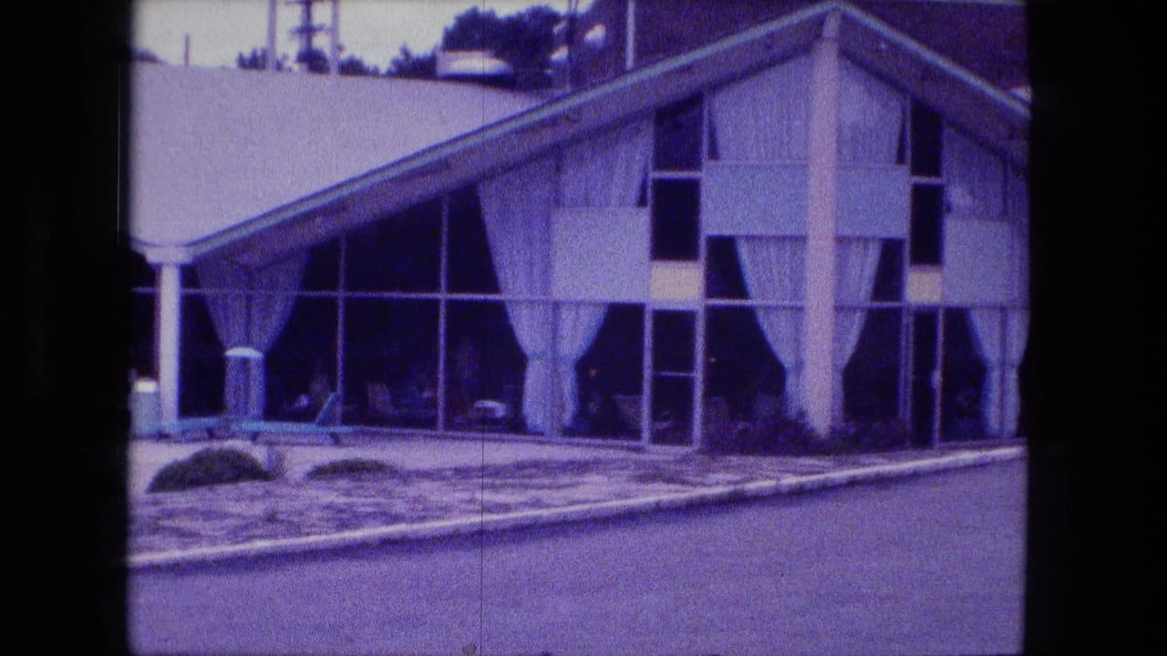 1974 Fort Wayne 8mm frame showing a modernist building with broad windows, white curtains, columns, shrubs, and a poolside foreground.