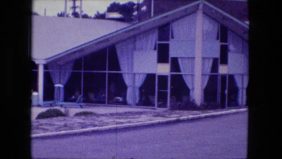 1974 Fort Wayne 8mm frame showing a modernist building with broad windows, white curtains, columns, shrubs, and a poolside foreground.