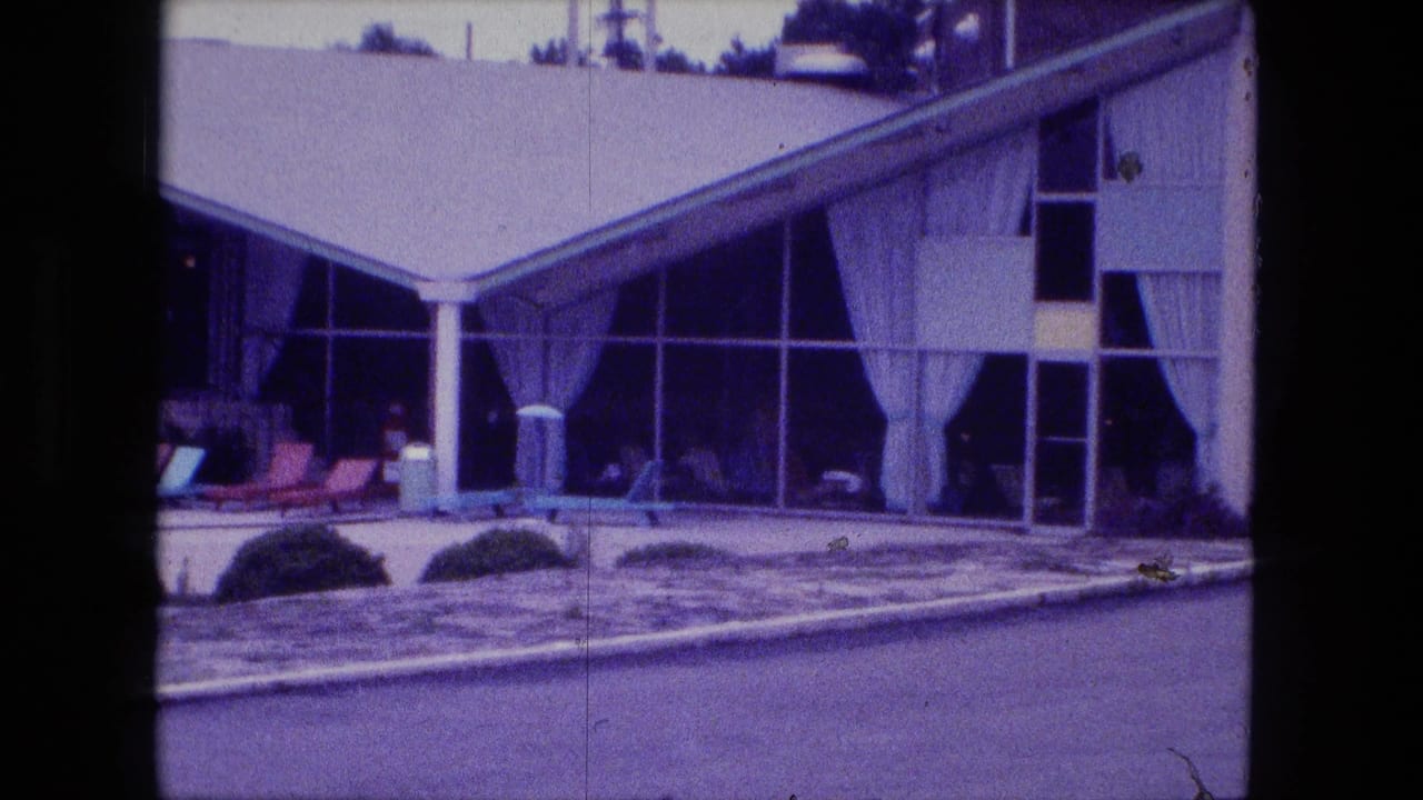 Glass-fronted building with curtains, patio furniture, pool edge, shrubs, and lounge chairs.