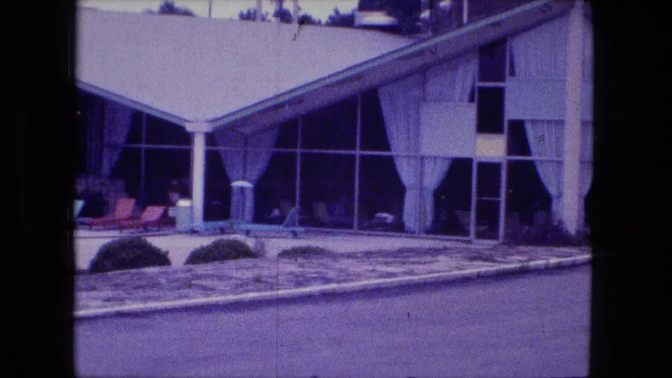 1974 Fort Wayne frame of the sloped-roof building, with window walls, curtains, columns, landscaping, and poolside paving visible.