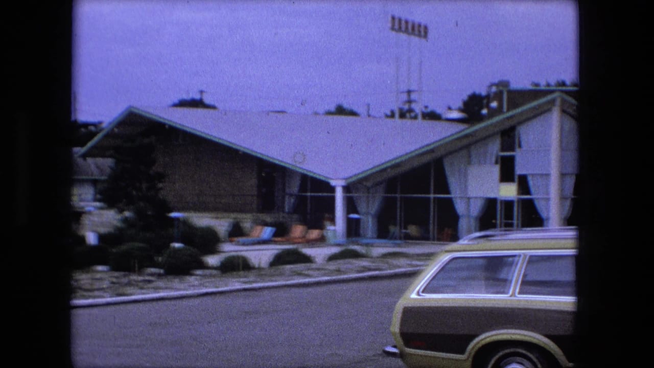 1974 Fort Wayne-area frame with a wood-paneled station wagon partly visible near a modern resort or motel exterior.