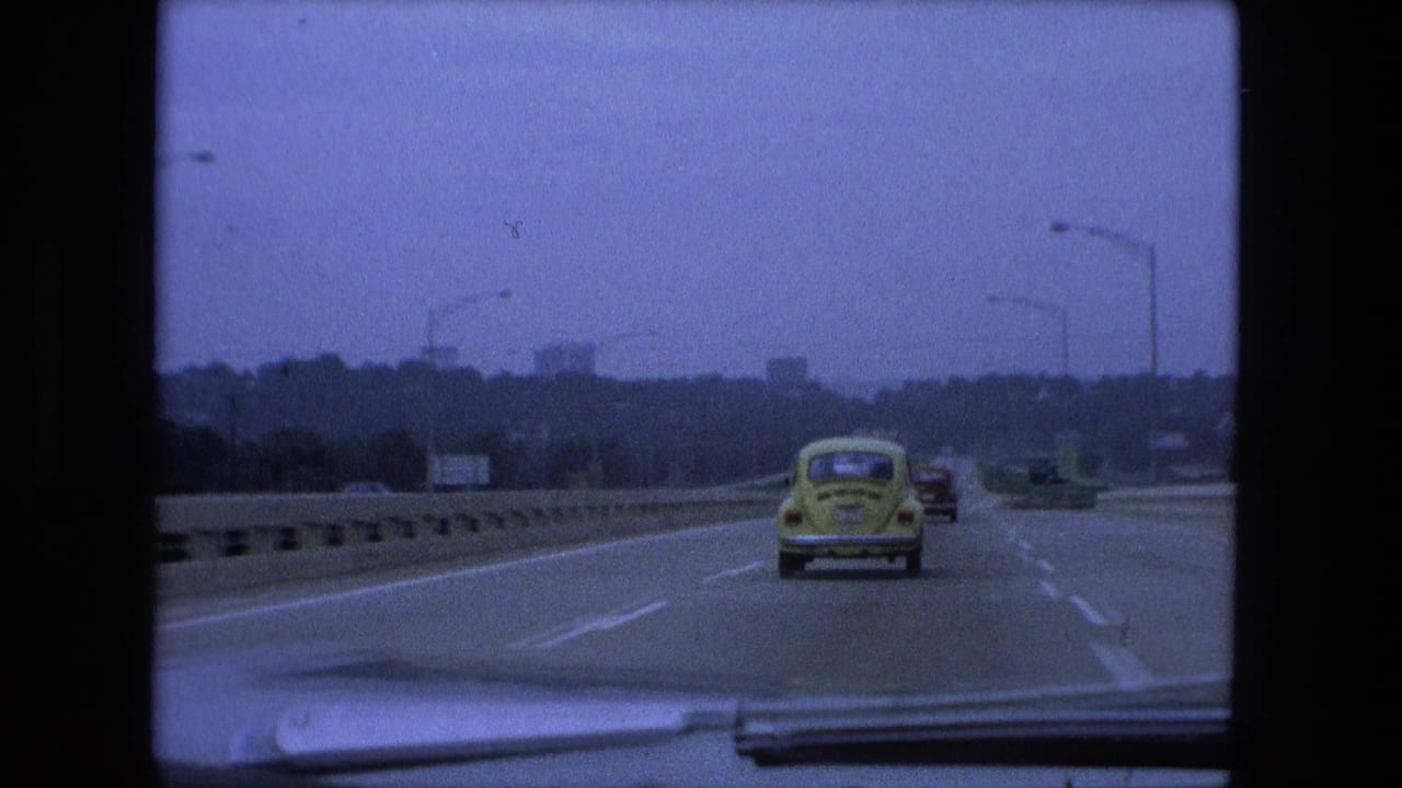 Yellow Volkswagen Beetle traveling ahead on a multi-lane highway with distant traffic.