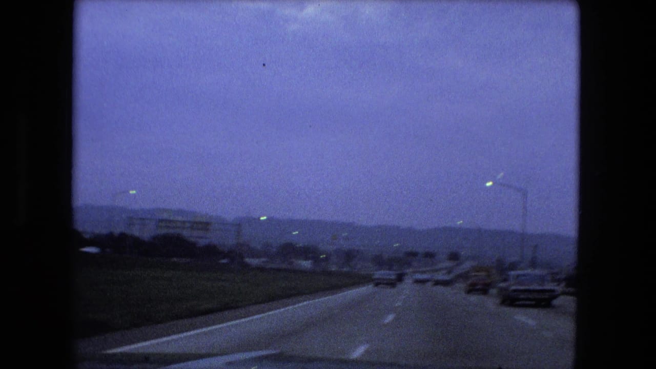 Passenger-view highway lanes with distant cars under an overcast sky.