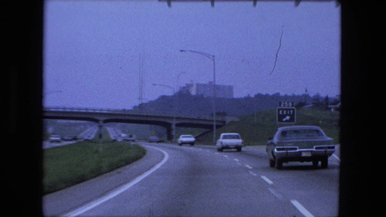 Cars travel on a multi-lane interstate toward an overpass and roadside exit sign.