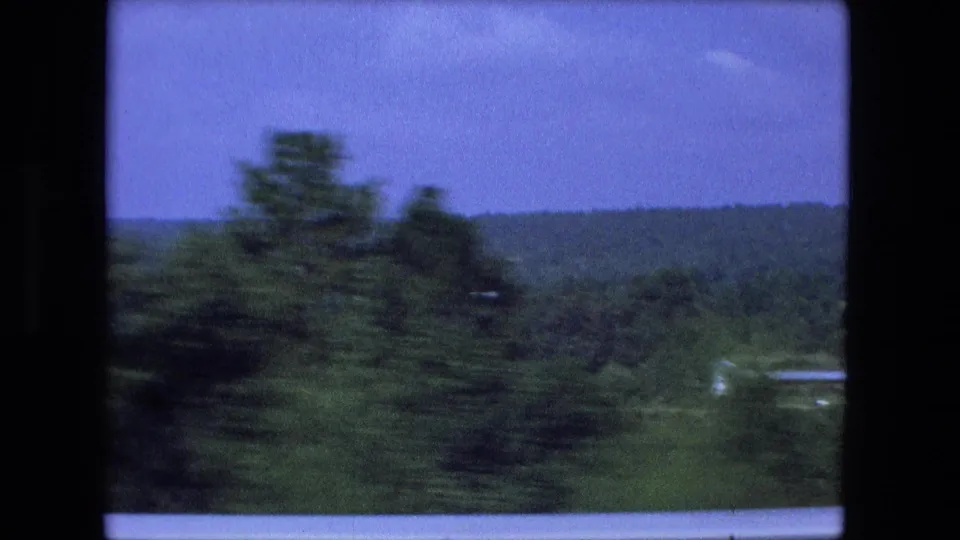 Motion-blurred trees pass in front of distant Indiana countryside during a 1974 8mm summer drive.