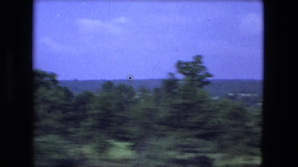 Green countryside near Fort Wayne with trees, distant houses, and low hills viewed from a moving vehicle in 1974.